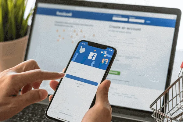 Facebook logo on mobile app infront of a laptop screen